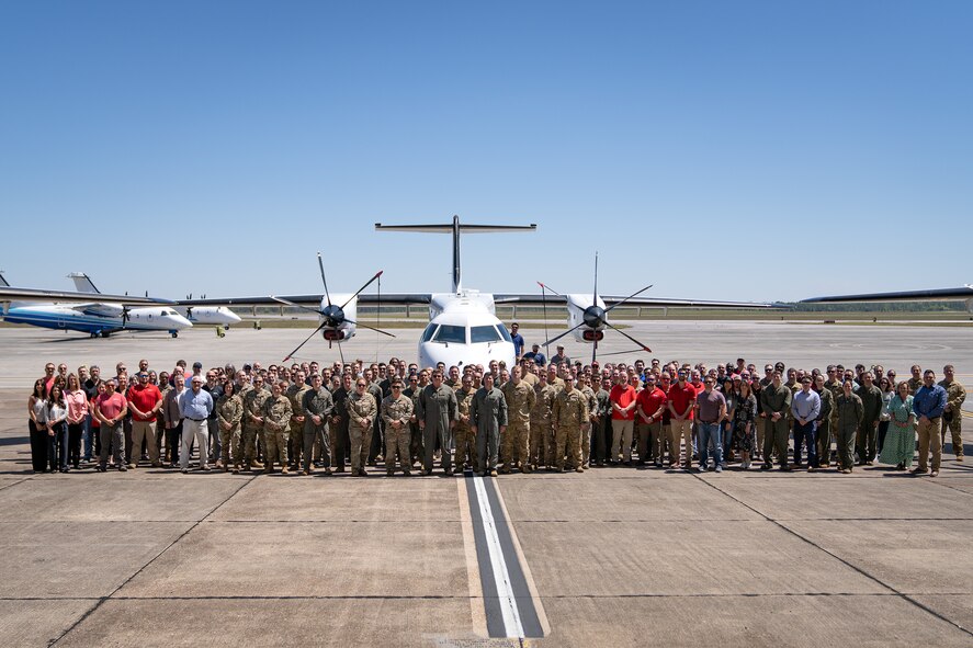 A large crowd of people stand on the flightline in front of several aircraft