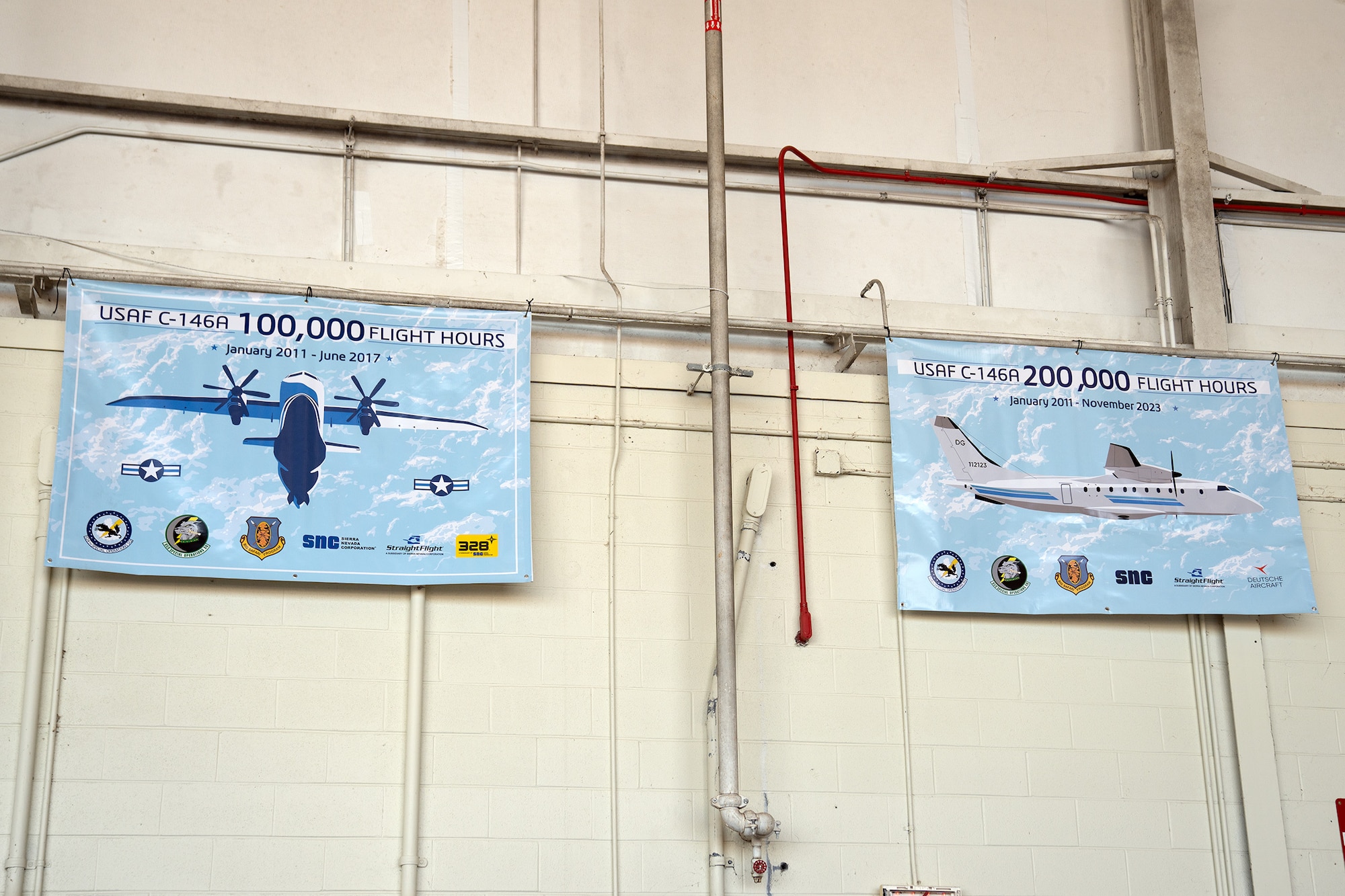 Two banners featuring aircraft demarcate milestones in flight hours and hang on a bare cement block wall