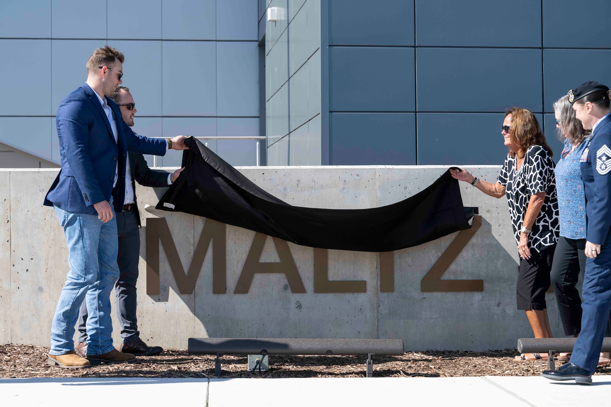 A group of people remove a cloth unveiling the official name of a new aquatic training center named after U.S. Air Force Master Sgt. Michael Maltz.