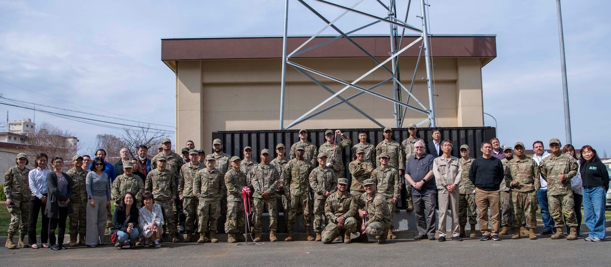 Military members, Japanese nationals, and civilians pose for a group photo in front of a tower.