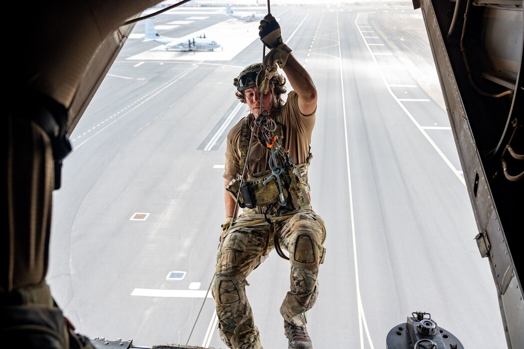 An Airman wearing combat gear begins repelling from an aircraft.