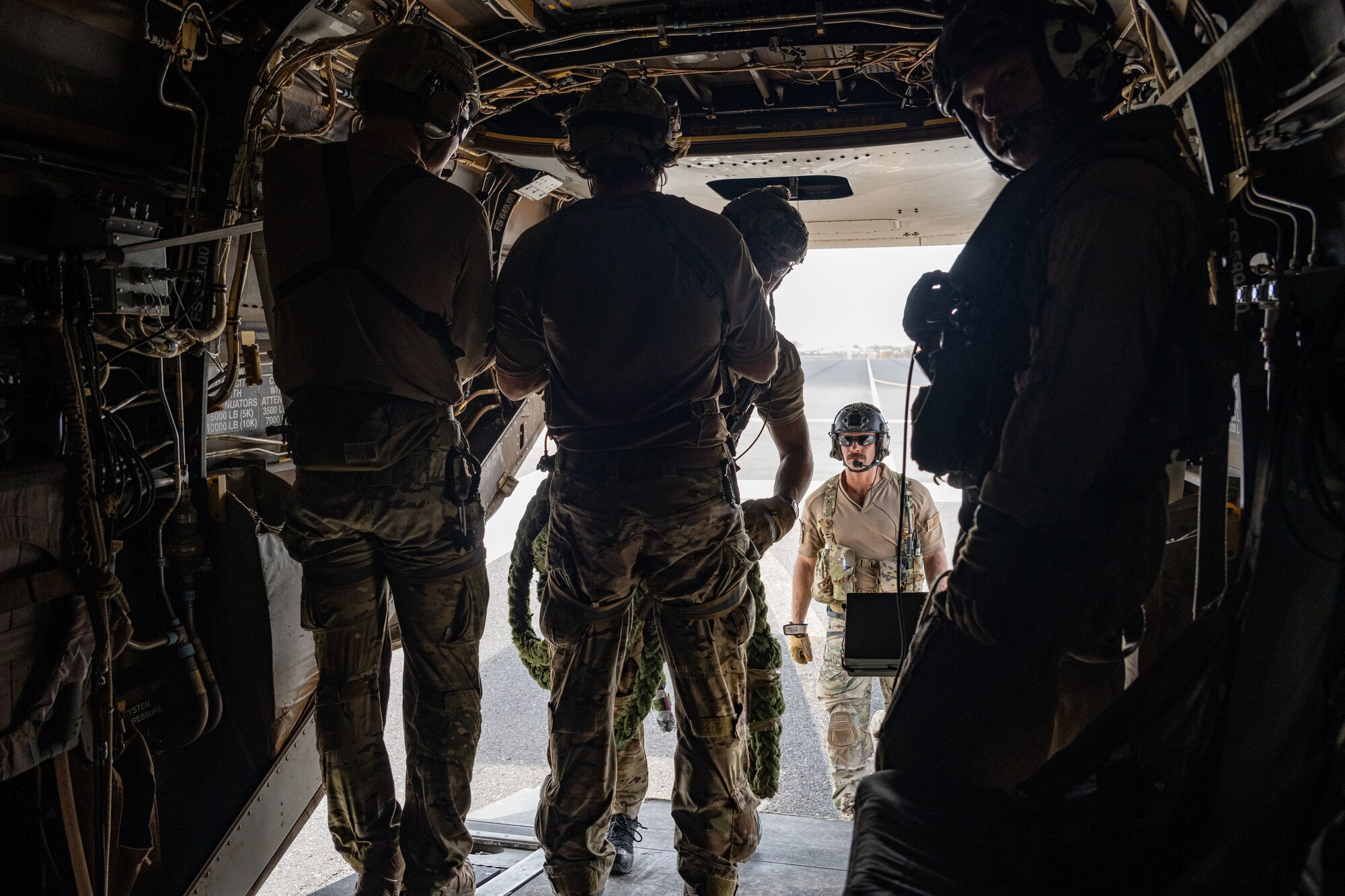 Four service members onboard an aircraft look out an aircraft cargo ramp as another prepares to board.