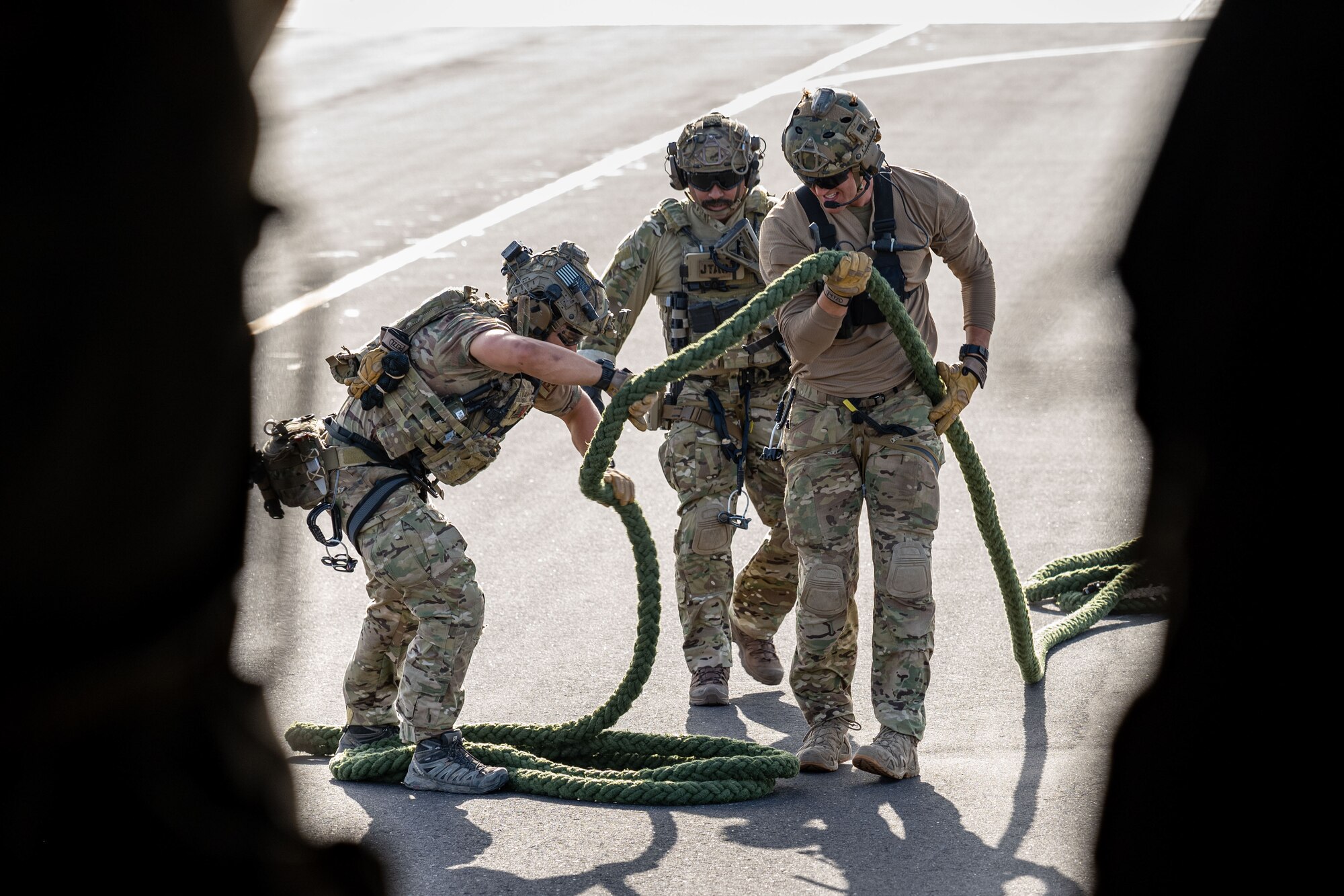 Three Airmen in uniforms hold a fast rope on a runway.
