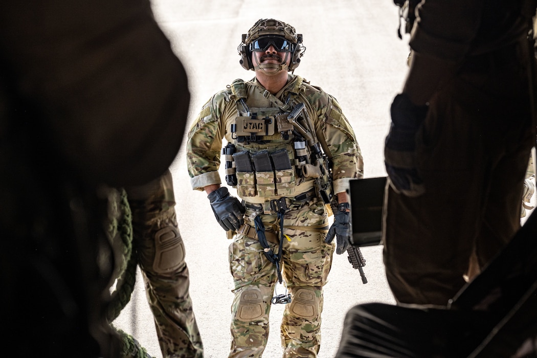An Airman wearing combat protective gear stands between two members as he prepared to board an MV-22 Osprey.