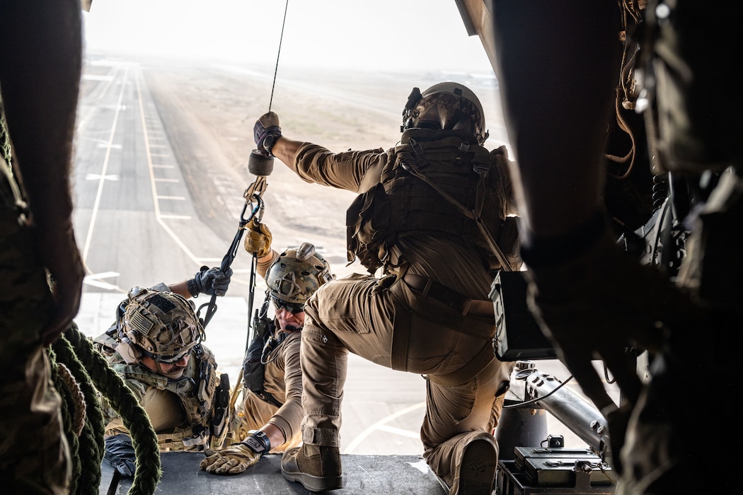 A Marine holds a cable hoisting two Airmen into an MV-22 Osprey aircraft.
