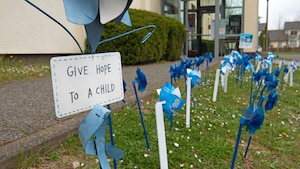 Pinwheels and a sign that reads "Give hope to a child" are displayed in a grass field in front of a building.