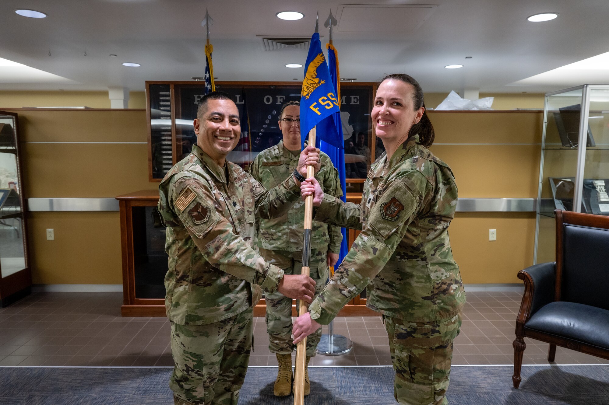 A man and woman in uniform pose for a photo holding a blue flag