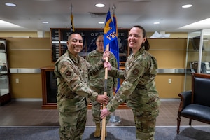 A man and woman in uniform pose for a photo holding a blue flag