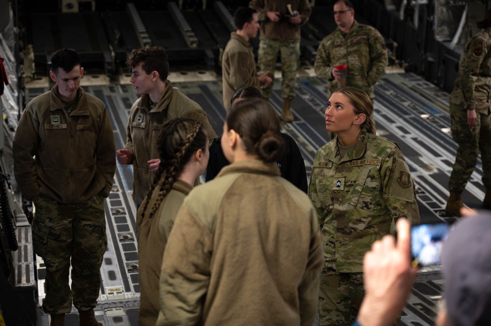 A group of people in uniform tour the back of a military cargo aircraft