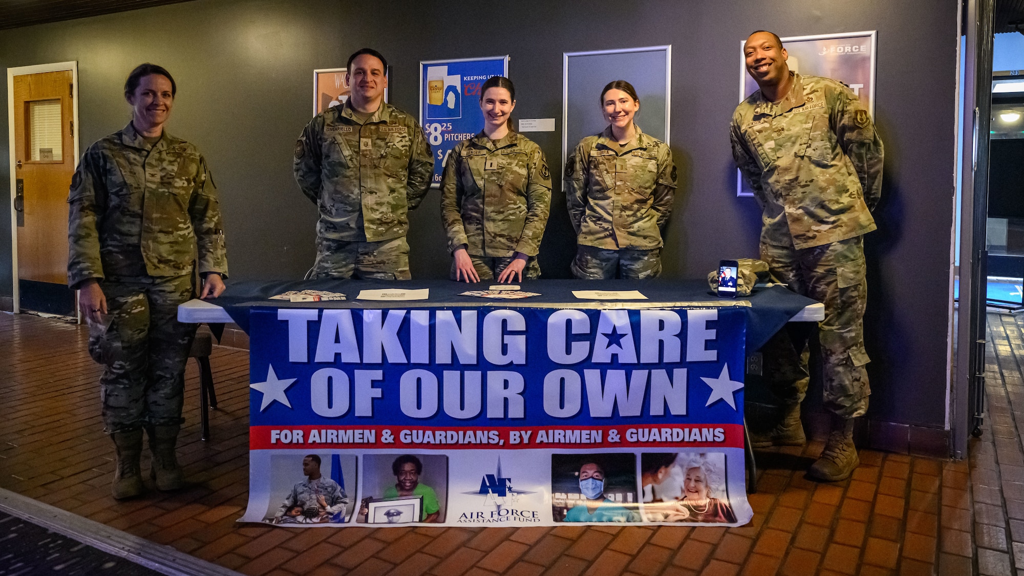 Wing leadership and AFAF project officers stand behind a table featuring an AFAF banner that reads Taking Care of Our Own.
