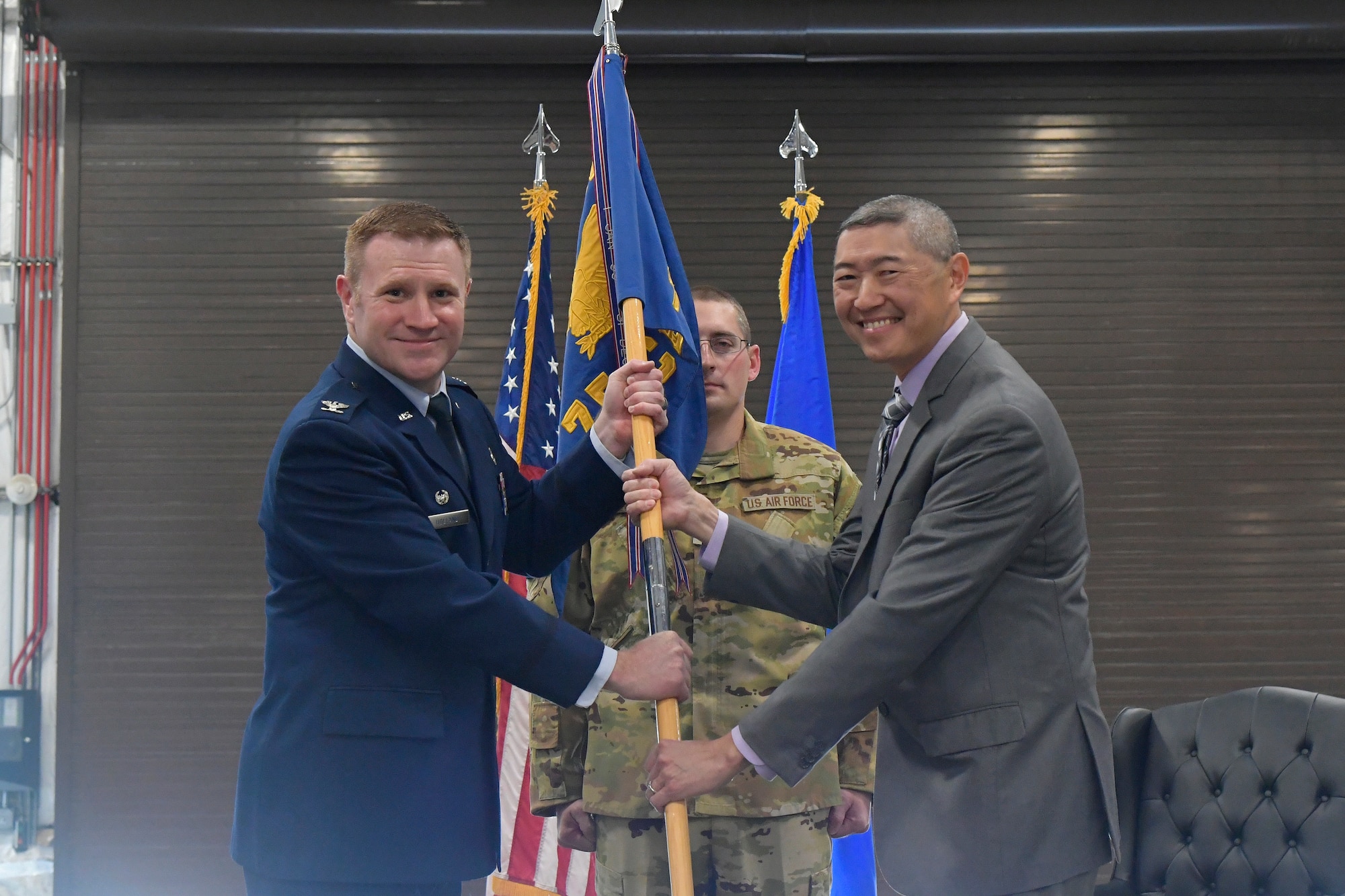 Peter Feng and Col. Holland stand, each with their hands on the guidon.