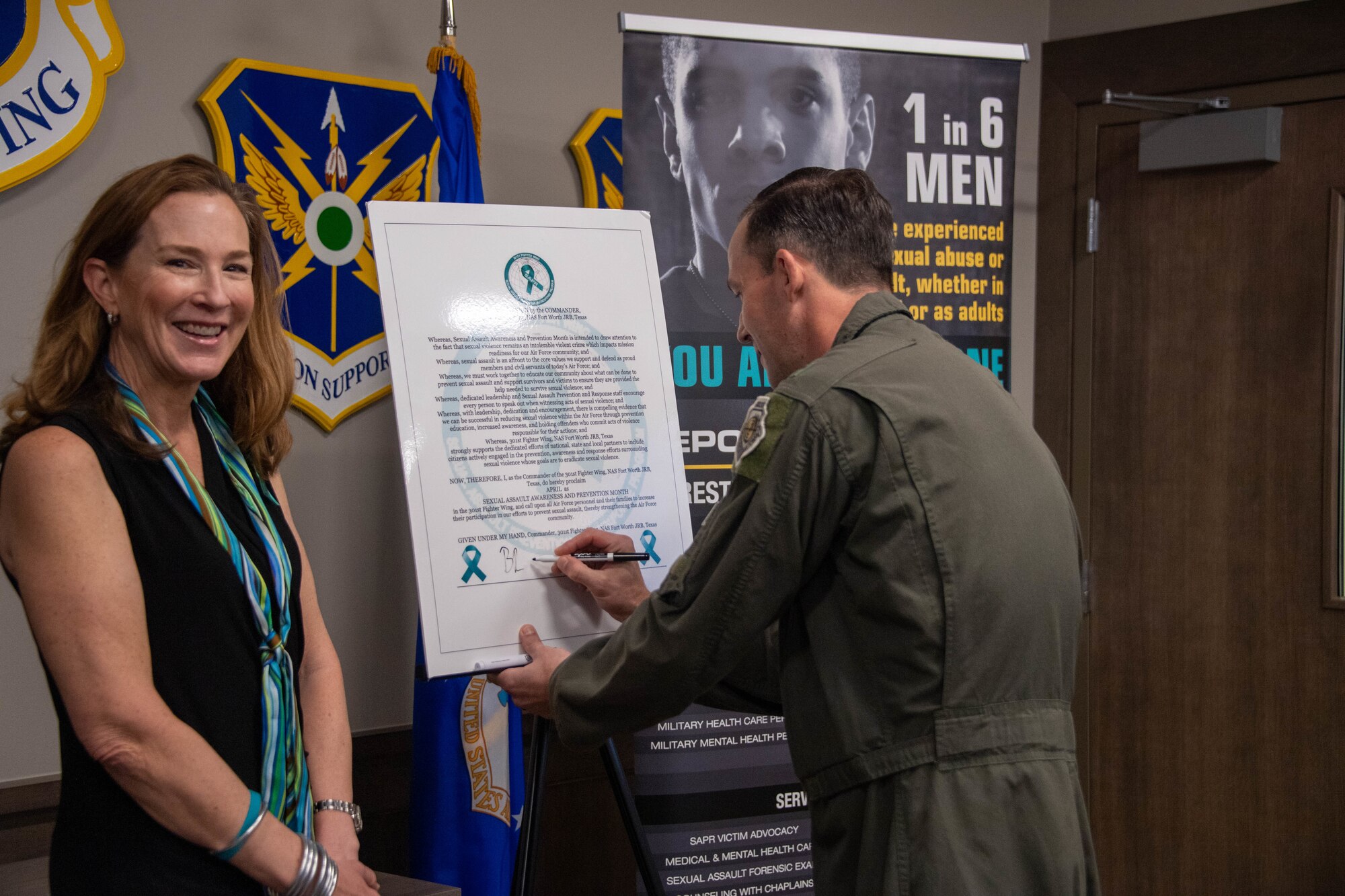 Col. Benjamin Harrison, 301st Fighter Wing commander(right) signs a proclamation in recognition of Sexual Assault Awareness and Prevention Month (SAAPM), alongside Laura Loftin, 301 FW sexual assault response coordinator at Naval Air Station Joint Reserve Base Fort Worth, Texas on April 5, 2024. (U.S. Air Force photo by Nije Hightower)