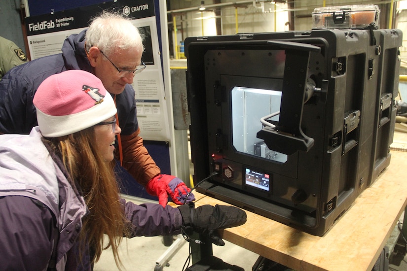 Two people wearing jackets and gloves look at a machine.