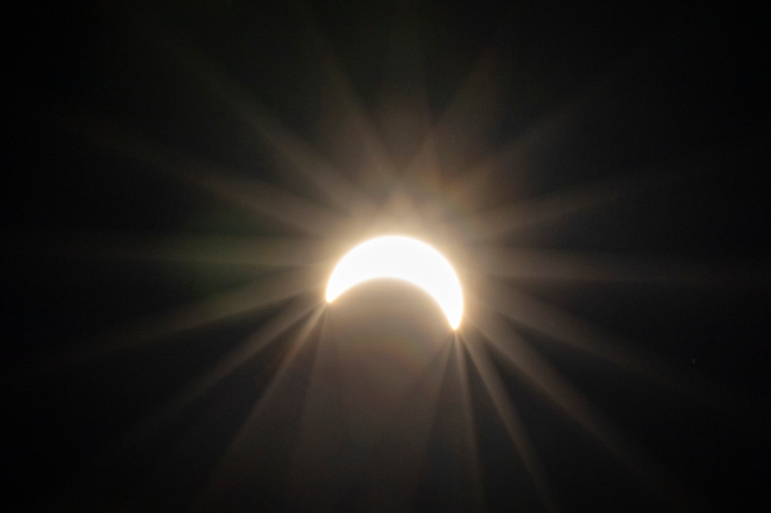 Glare radiates around a partial solar eclipse against a dark background.