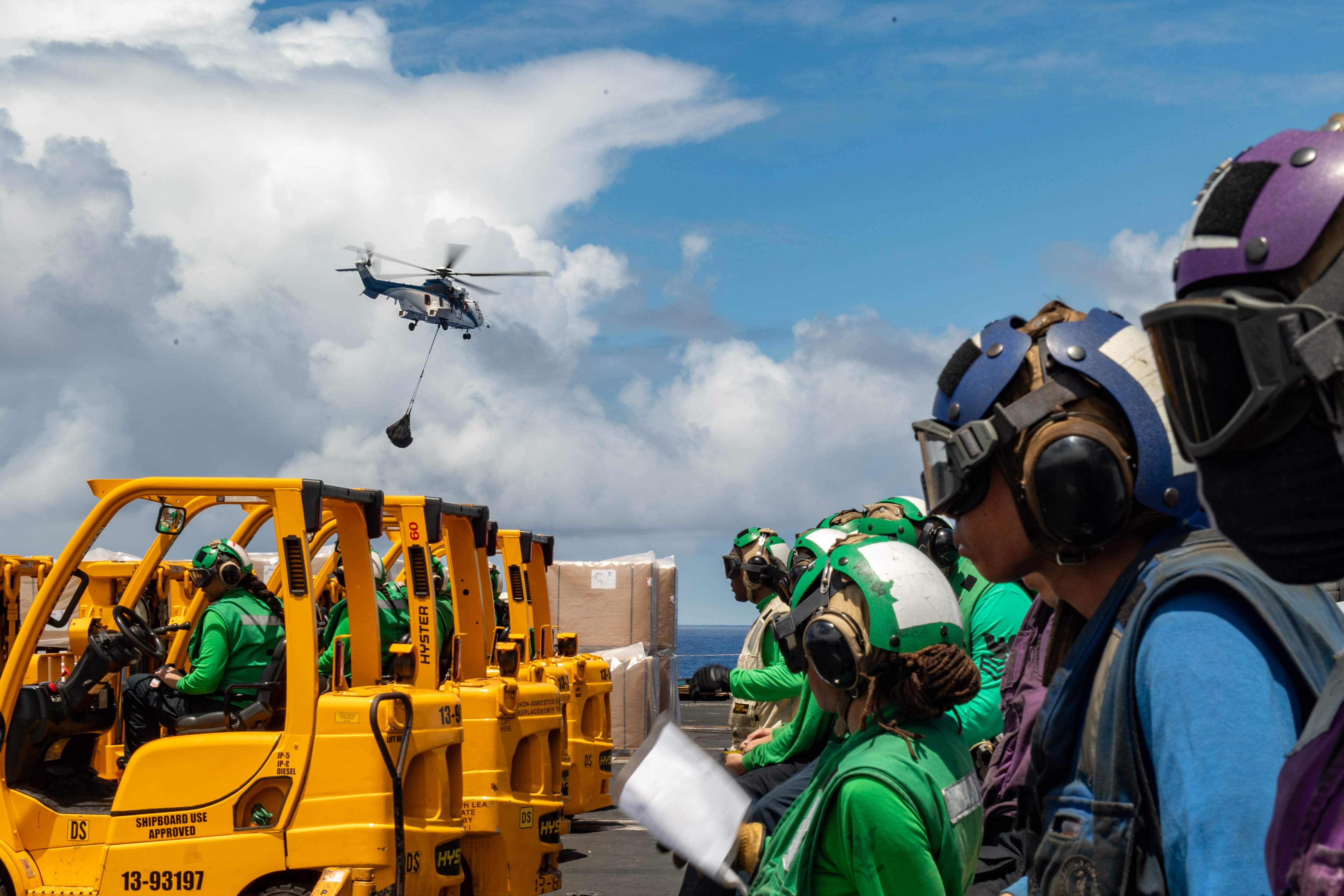 U.S. Sailors watch an AS-332 Super Puma and Clark-class dry cargo ship USNS Wally Schirra (T-AKE 8), fly over the Nimitz-class aircraft carrier USS Theodore Roosevelt (CVN 71)