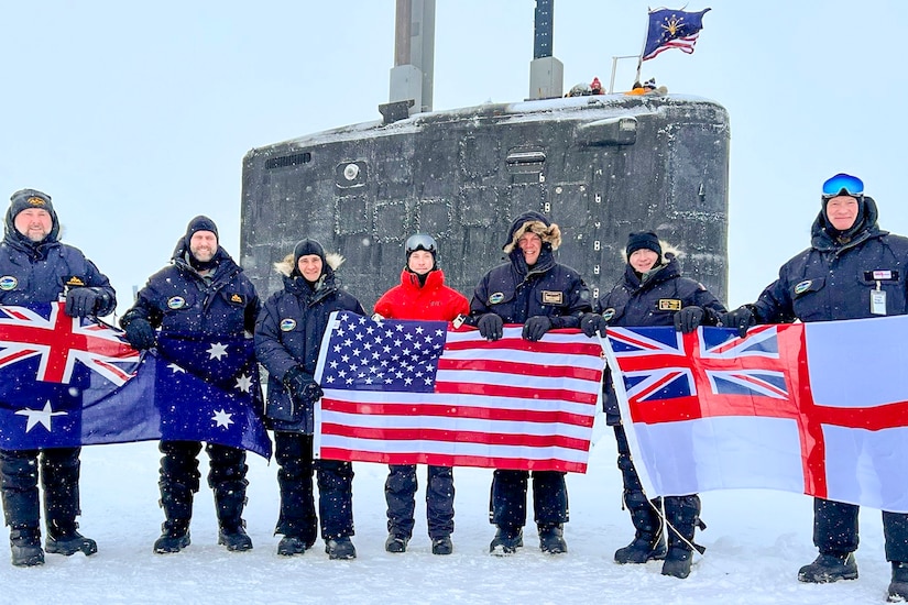 Seven people, bundled for the cold, stand in the snow holding three, large flags.