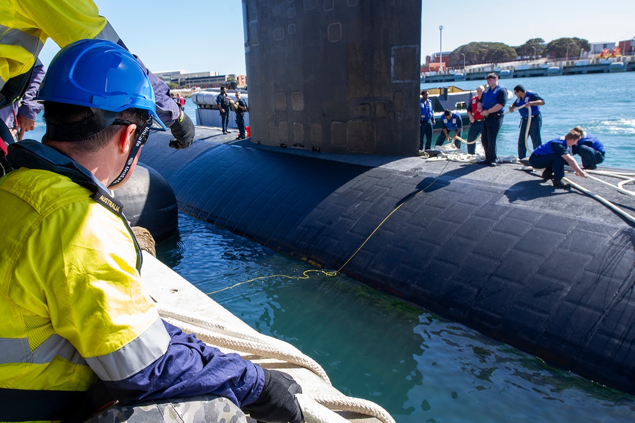 Sailors handle mooring lines aboard a submarine as Australian crew members observe.