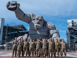 A group of Airmen from Dover Air Force Base pose in front of the “Miles the Monster” statue at Dover Motor Speedway, Dover, Delaware, April 8, 2024. The model car, which celebrates the relationship between the speedway and Dover AFB, was lifted to be displayed in the statue’s grip. (U.S. Air Force photo by Airman Liberty Matthews)