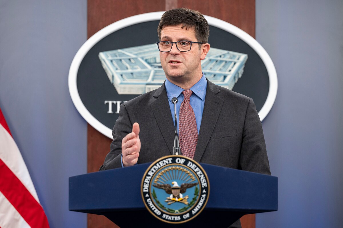 A person wearing a suit stands at a lectern.
