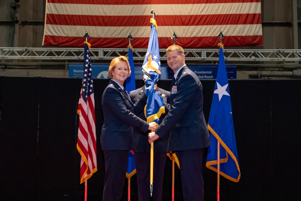 A smiling woman in uniform passes a guidon to a smiling man in uniform.