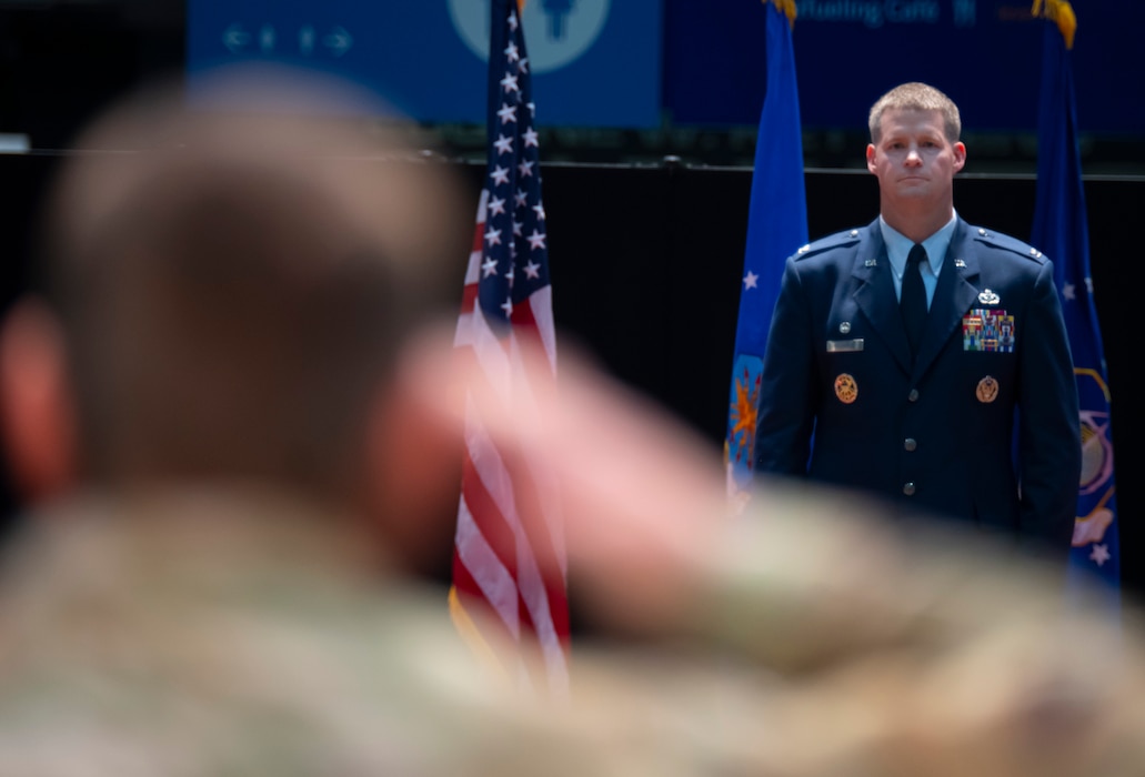 Man in blue uniform stands facing a man in a green uniform saluting him.