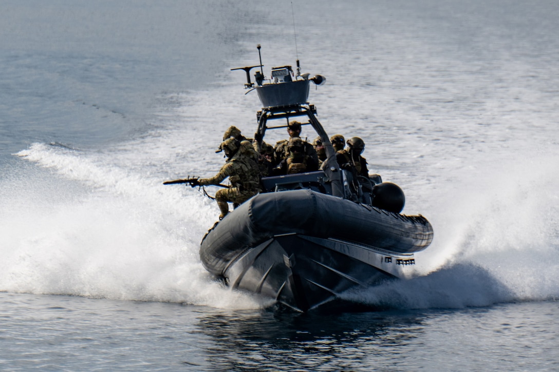 An inflatable vessel carrying service members creates a wake. One of the military members holds a weapon.