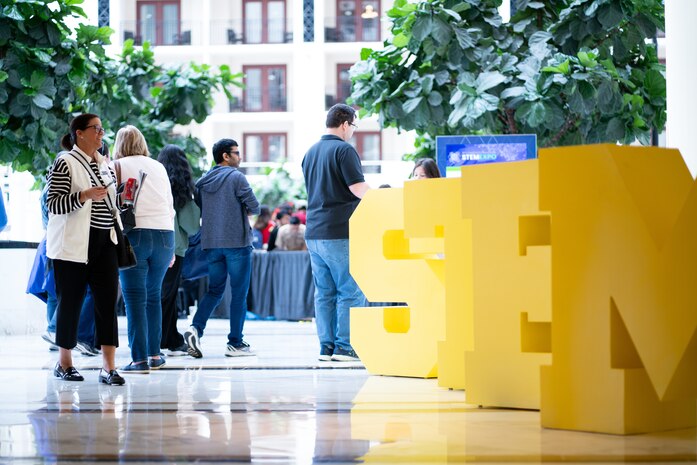 Attendees enter the main exhibit area for the Sea-Air-Space Science, Technology, Engineering, and Math (STEM) expo at the Gaylord National Hotel and Conference Center, Sunday. The entrance to the exhibits was lined with large-sized yellow letters S T E and M as a welcome to the expo. Conference goers had the opportunity to participate in hands-on science activities and experience interactive exhibits based on STEM concepts with more than 20 exhibitors from various Department of Defense service branches.