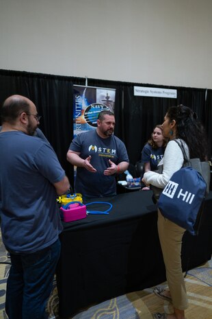 Dr. Greg Bouton (center) talks about the mission of the U.S. Navy's Strategic Systems Programs (SSP) and how Science, Technology, Engineering, and Math activities are connected to the real-world missions of commands like SSP during the Sea-Air-Space STEM expo at the Gaylord National Hotel and Conference Center, Sunday. Conference goers had the opportunity to participate in hands-on science activities and experience interactive exhibits based on STEM concepts with more than 20 exhibitors from various Department of Defense service branches. SSP is the Navy command that is responsible for the cradle-to-grave lifecycle of the submarine-launched ballistic missile system.