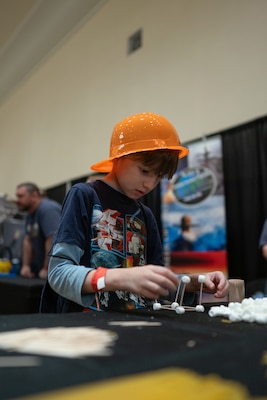 An elementary-aged student tests his ability to build a structurally sound shape with toothpicks and marshmallows to demonstrate basic engineering competencies during the Sea-Air-Space Science, Technology, Engineering, and Math (STEM) expo at the Gaylord National Hotel and Conference Center, Sunday. The activity was hosted by the U.S. Navy's Strategic Systems Programs (SSP) to connect young learners' proficiencies in STEM activities to elements of the real-world missions of commands like SSP.  SSP is the Navy command that is responsible for the cradle-to-grave lifecycle of the submarine-launched ballistic missile system.