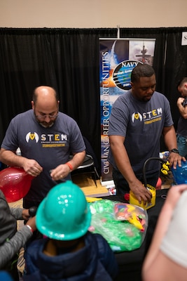 Volunteers Adam Allex (left) and Nicolas Tarver (right) from U.S. Navy Strategic Systems Programs (SSP) attach balloons to 3-D rocket boosters in order to demonstrate Newton's Third Law of Motion during the Sea-Air-Space Science, Technology, Engineering, and Math (STEM) expo at the Gaylord National Hotel and Conference Center, Sunday. SSP's STEM learning activities connected young learners' proficiencies in STEM activities to elements of the real-world missions of commands like SSP.  SSP is the Navy command that is responsible for the cradle-to-grave lifecycle of the submarine-launched ballistic missile system.