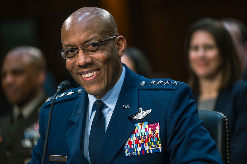 A smiling man in military dress uniform sits with a microphone in front of him.