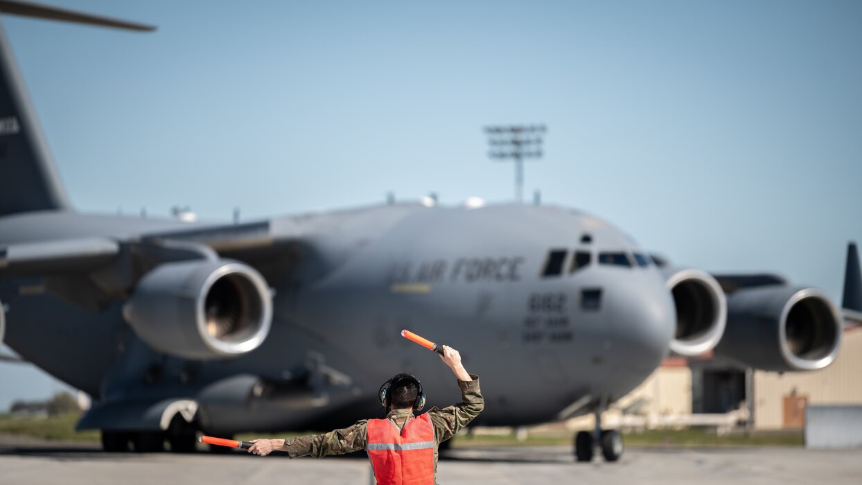 A crew chief directs a C-17 Globemaster III to its parking spot