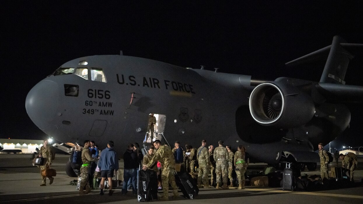 A group of Airmen greet and unload equipment outside a C-17 Globemaster III aircraft