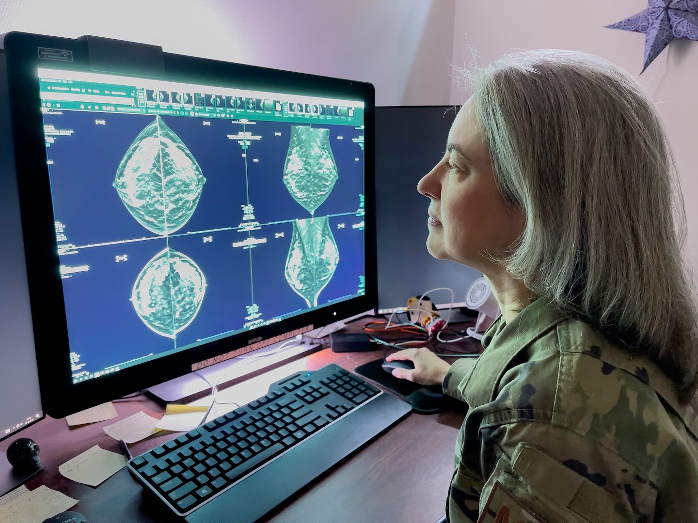 Female Uniformed Service Member looks at mammogram images on a monitor with a keyboard.