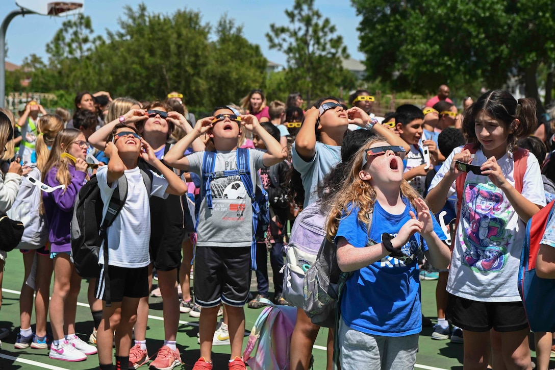 A group of students wearing eclipse glasses look up at the sky.