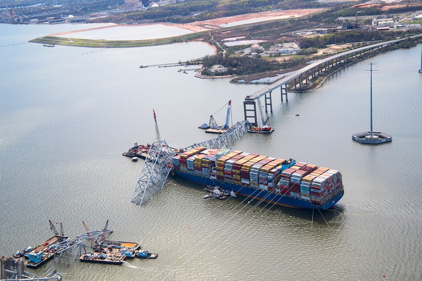 An aerial image of a container barge in water amid wreckage from a collapsed bridge.