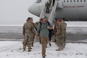 Airmen walk down the steps to get off the plane while it's snowing and are greeted by other Airmen.
