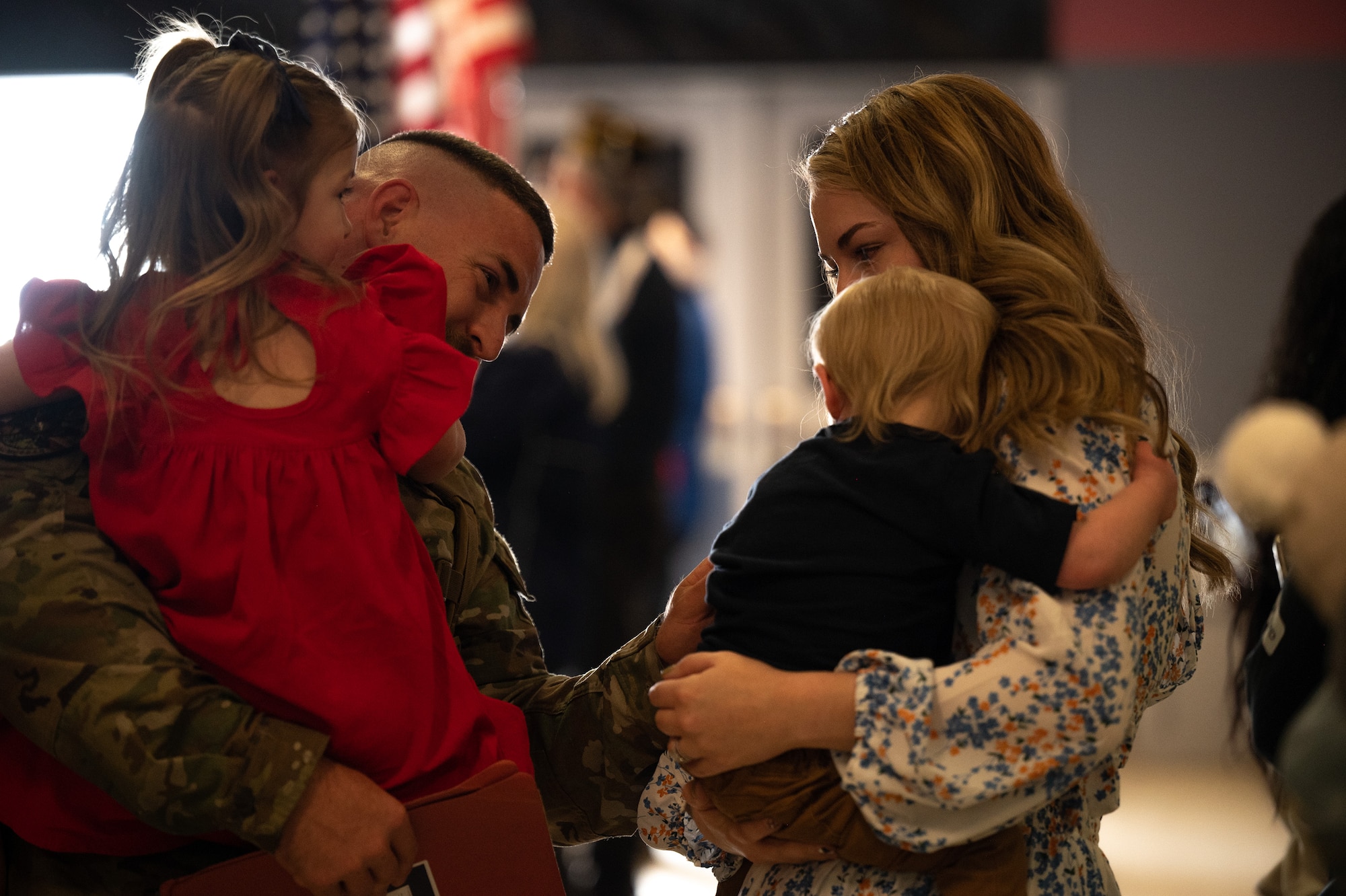 An Airman holds his daughter and reaches touches his son's face who his wife is holding beside him during a family reunion.