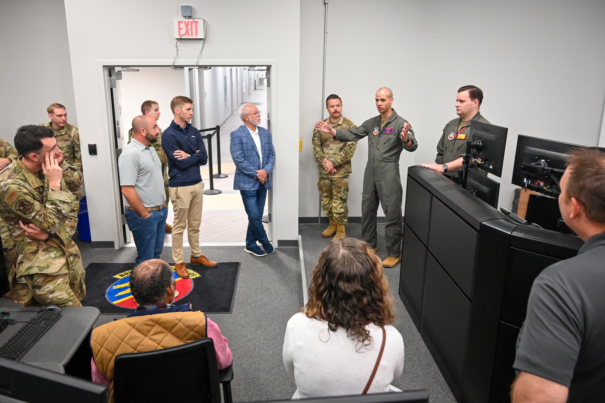Military personnel and civilians listen to a brief in an operations room.
