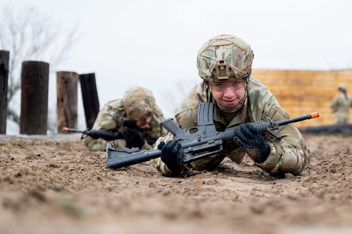 A Security Forces technical training student holds her weapon as she crawls during training at Joint Base San Antoino-Chapman Annex, Texas, Jan. 22, 2024. The 343rd Training Squadron is optimizing training to ensure Defenders are equipped with the skills and knowledge needed to tackle evolving threats in a modern era. The 343 TRS Security Forces technical training is one of the key components in the Defender Next initiative, where the career field is undertaking the largest shift in the schoolhouse in over two decades.  (U.S. Air Force photo by Vanessa R. Adame)