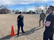 student holds baton in an outside training scenario while instructor talks to them.