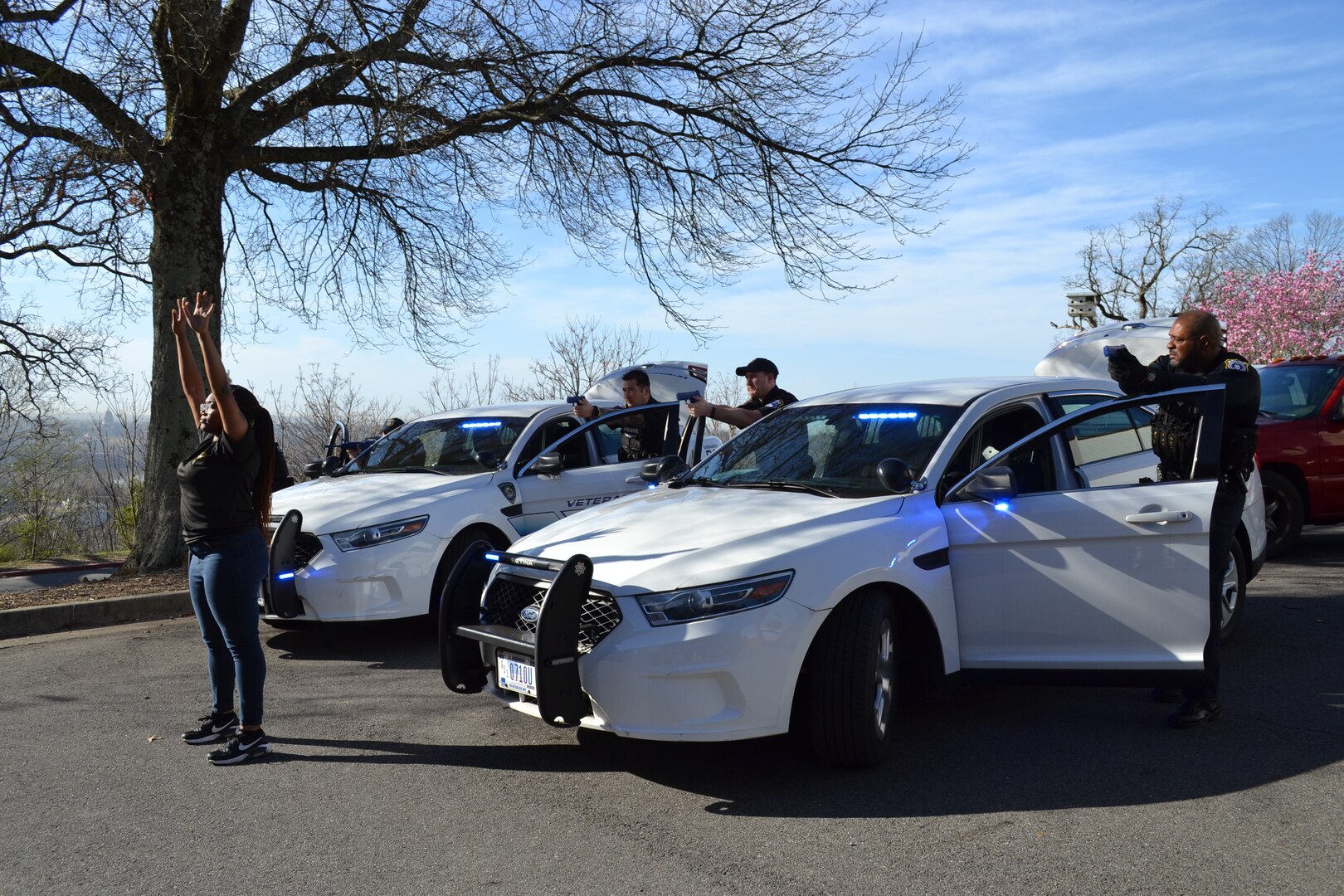 "Suspect" holds up hands while civilian Defenders position themselves behind car doors with weapons drawn.