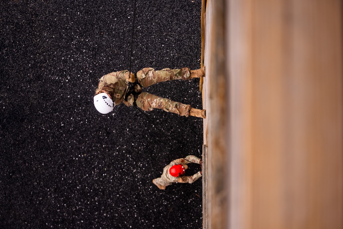U.S. Air Force Officer Training School trainee, top, rappels down a wall on the Blue Thunder obstacle course as part of their third training module, at Maxwell Air Force Base, Alabama. Capt. Patrick Francis, an OTS Instructor and the belay man on the ground, is serving as an added safety measure during these physically demanding and dangerous obstacles.