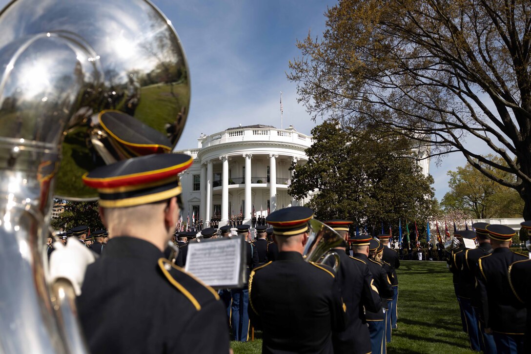 Soldiers in formal uniforms stand in formation playing musical instruments at the White House.