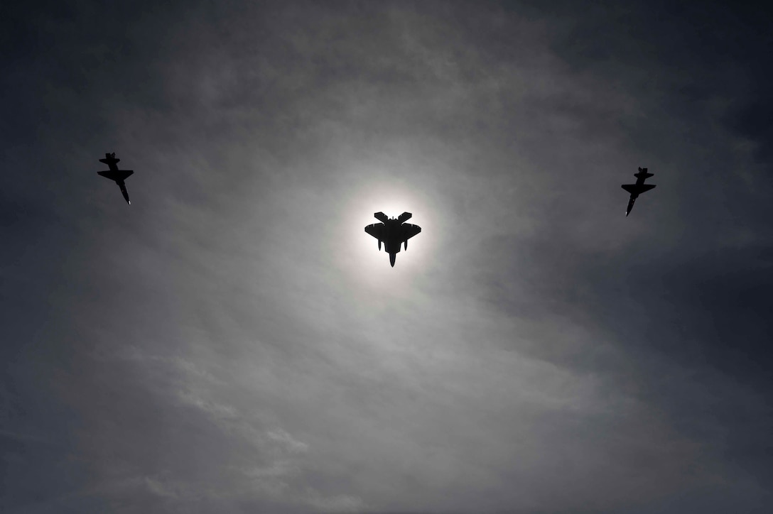 Three military aircraft fly in formation in a dark cloudy sky.