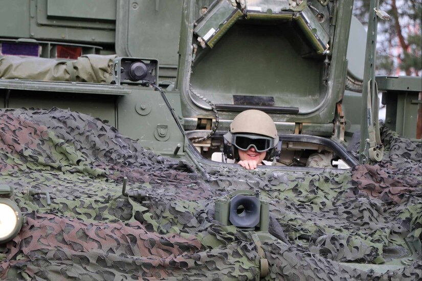 A soldier wearing a helmet peeks out from behind lots of camoflauge.