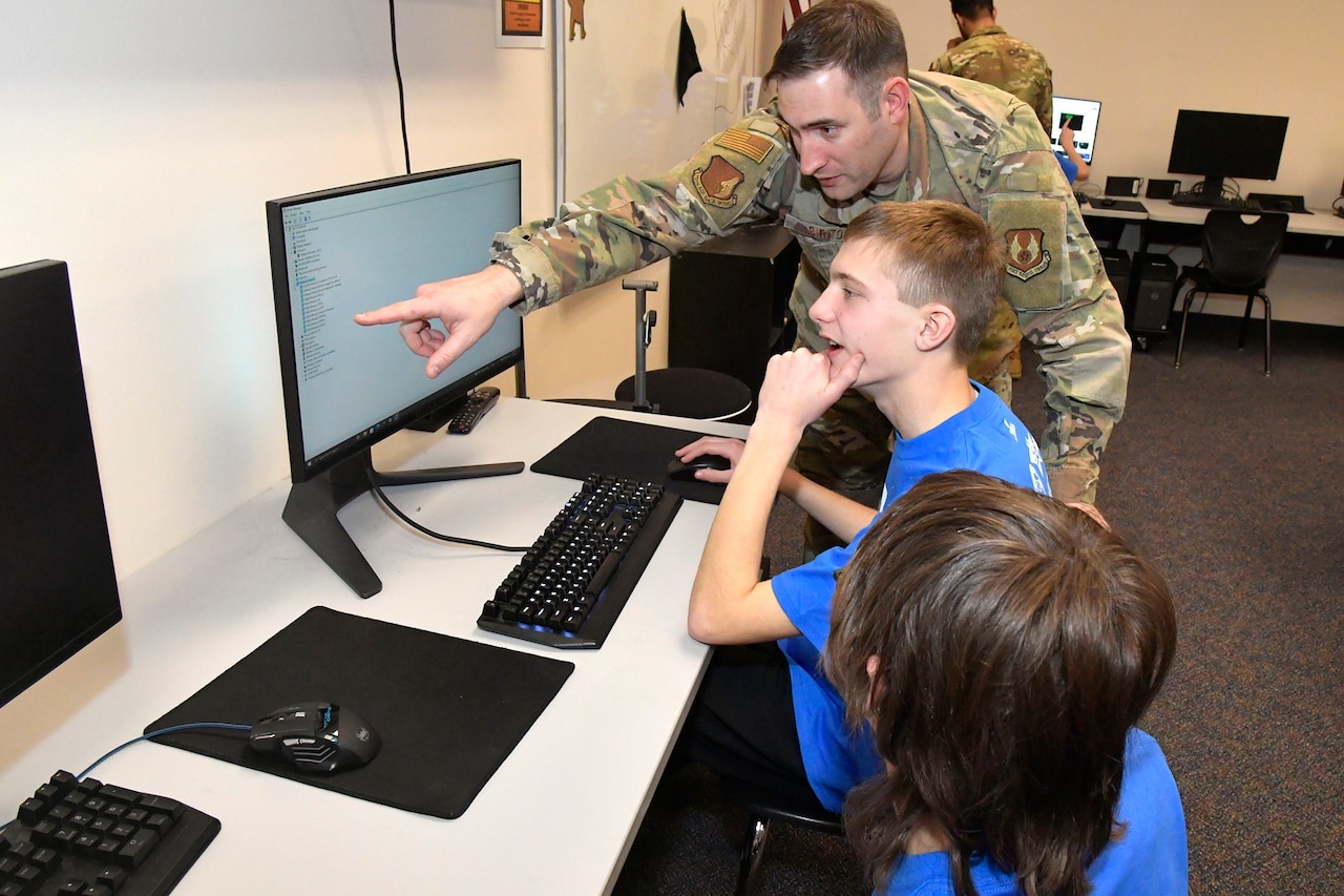 A service member and two children operate a computer.