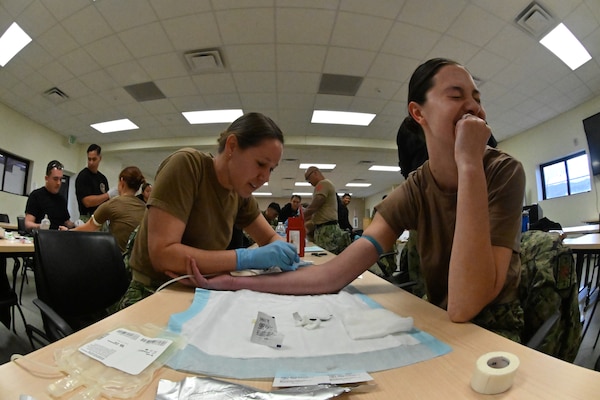 LCDR Michelle Caskey (left), and LT Carrigan Horton (right) assigned to Emergency Resuscitative Surgical System (ERSS) Bravo practice intravenous puncture and blood product collection from each other as part of an Operational Readiness Evaluation (ORE) of Navy EXMED capabilities at Naval Expeditionary Medical Training Institute (NEMTI), March 13. NEMTI staff teach the importance of a walking blood bank in the curriculum of all of Navy EXMED systems which allows anyone to be called upon to donate blood to those wounded in an austere and contested environment and allows for maximum survivability of the warfighter. ERSS is one of the Navy’s expeditionary medicine capabilities that provides a ready, rapidly deployable and combat effective medical forces to improve survivability across the full spectrum of care, regardless of environment. and provides targeted lifesaving interventions to patients onboard platforms and in austere environments without clinically compromising the patients’ condition. The Navy Medicine Operational Training Command (NMOTC) is the Navy’s leader in operational medicine and trains specialty providers for aviation, surface, submarine, expeditionary, and special operations communities. (U.S. Navy photo by Mass Communication Specialist 1st Class Russell Lindsey SW/AW)