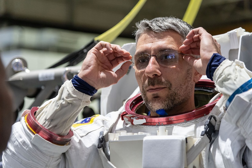 A person in a spacesuit adjusts their glasses.