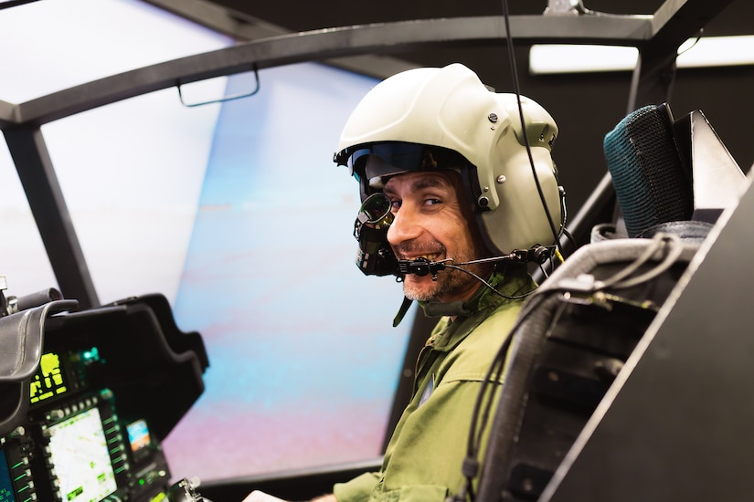 A person wearing a large helmet sits in front of a simulator consul.